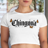 Woman wearing a white t-shirt with 'Chingona' printed on it, standing in front of a blurred outdoor background.
